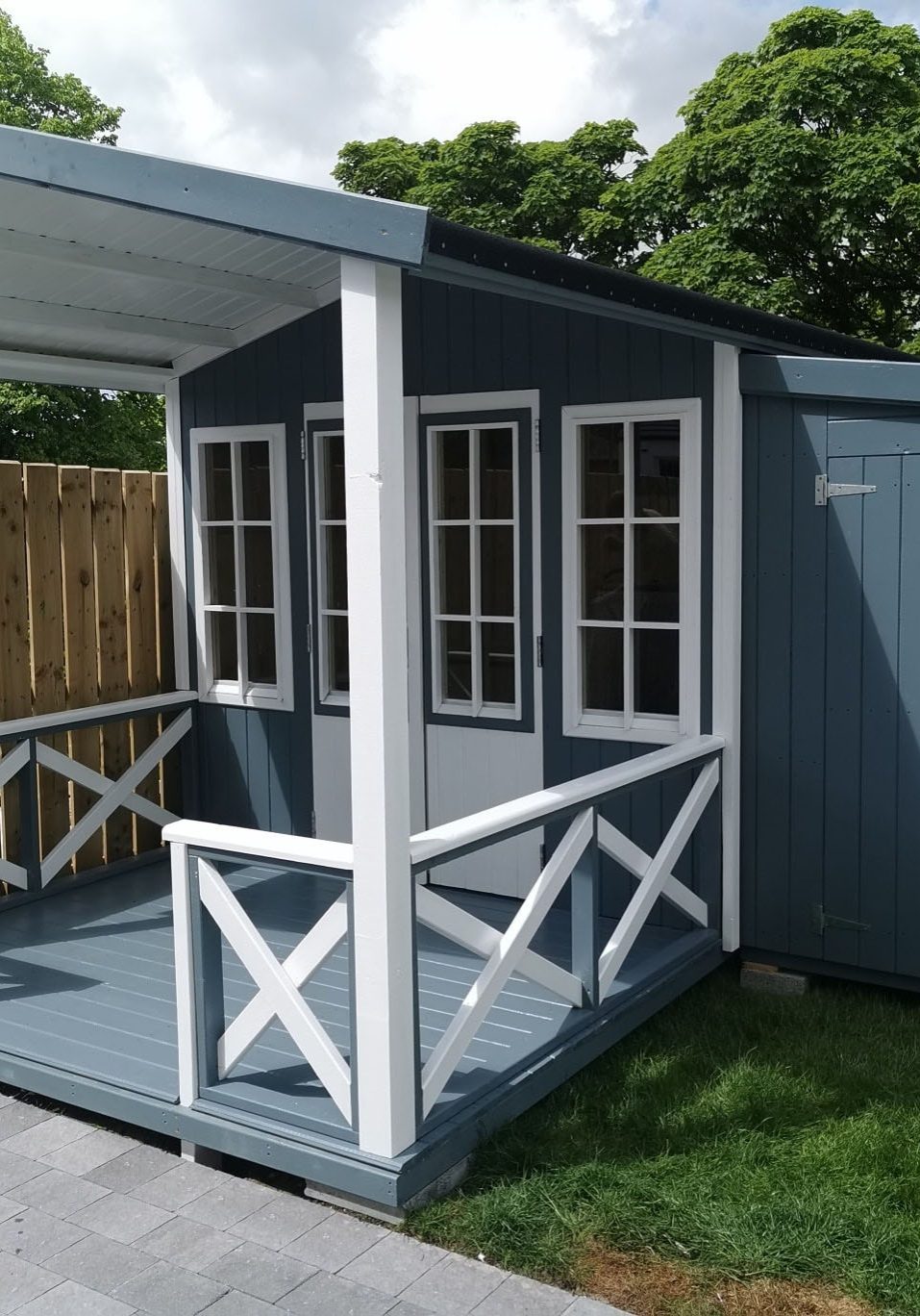 An image of a blue grey garden shed with a patio and French doors.